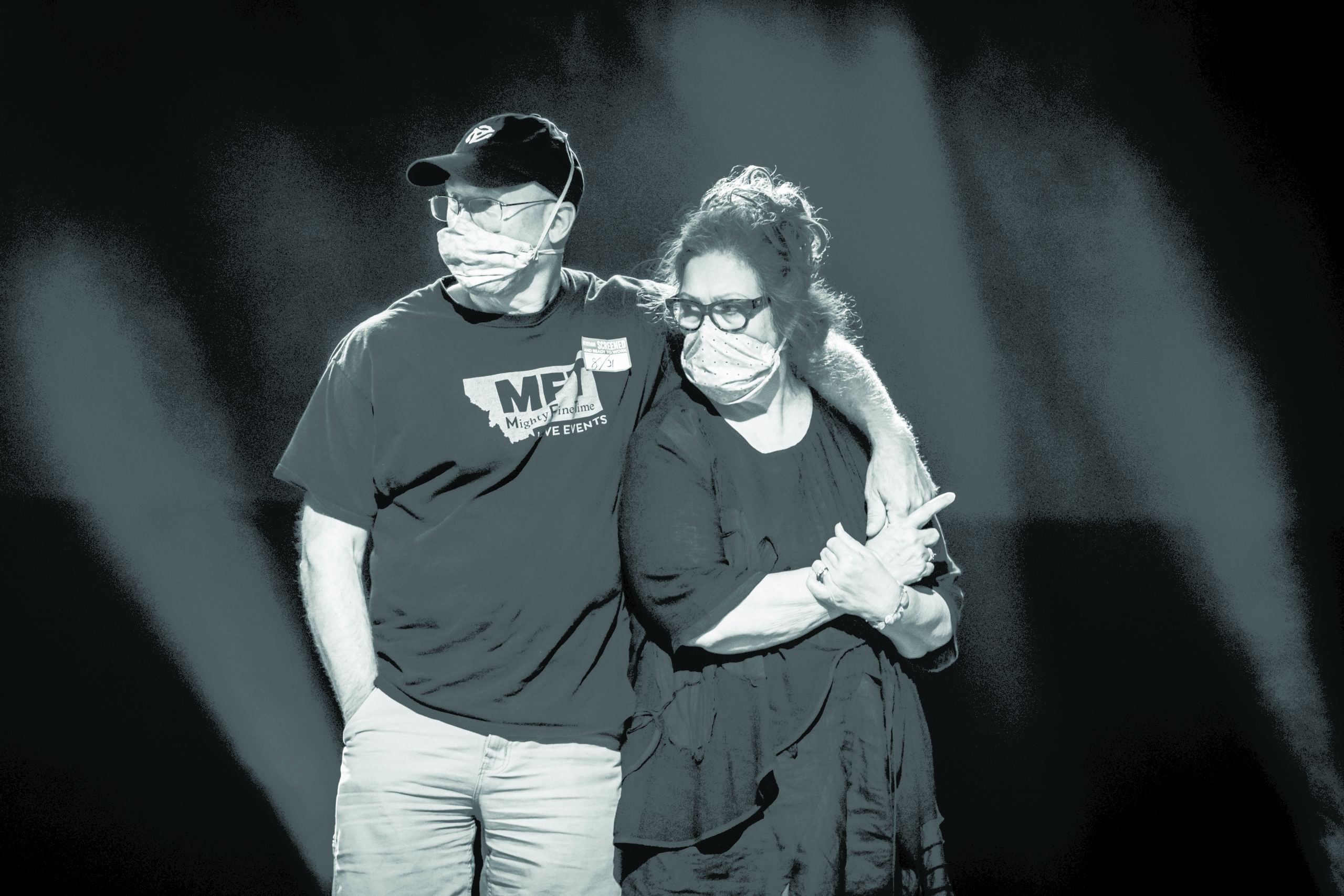John Lowell and Joanne Gardner stand on stage with face masks over mouth and nose
