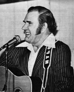 Hylo performing on stage with his guitar while singing.